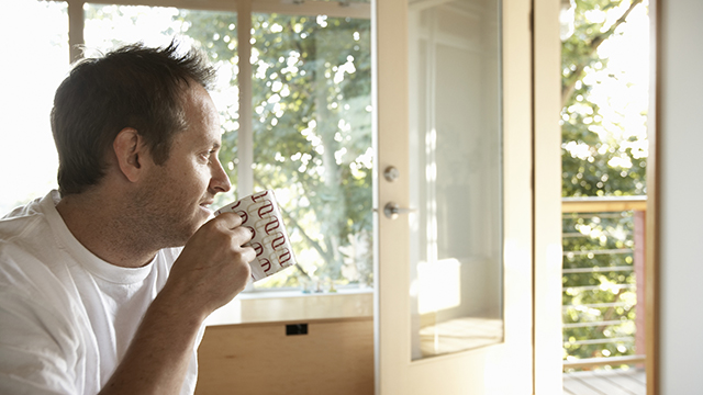 Man sitting indoors, drinking cup of coffee, side view